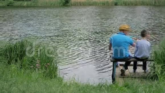 小儿子和爸爸在湖边的长凳上钓鱼视频的预览图