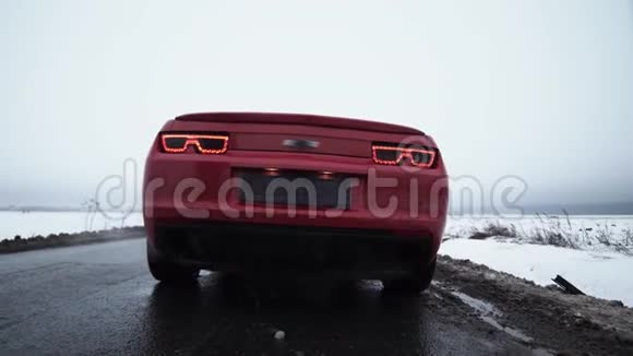 红肌肉汽车开始在被雪覆盖的田野包围的道路上行驶视频的预览图