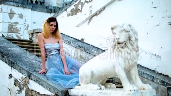 迷人的女孩黑色的眉毛和卷曲的头发银色和蓝色的裙子坐在石栏杆附近的狮子雕像和卷发视频的预览图