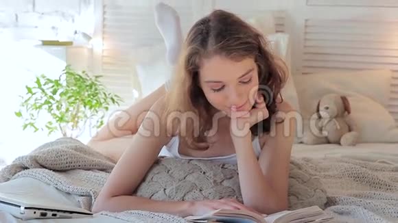早上躺在床上微笑着看书的年轻女子视频的预览图