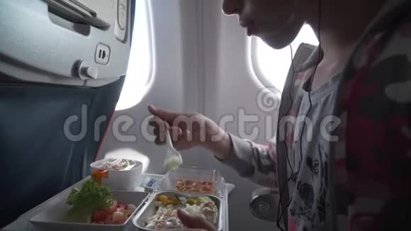 戴着耳机的年轻女孩正在飞机上吃美味的晚餐视频的预览图