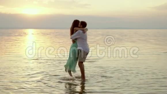 年轻快乐的男人在日落时分在海滩上抱起他的女朋友视频的预览图