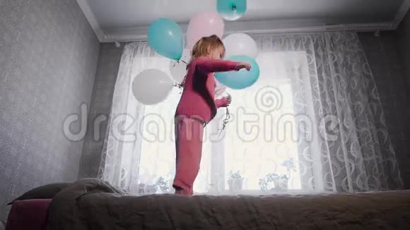 快乐的小女孩在托儿所的床上靠窗跳着手里拿着一堆气球视频的预览图