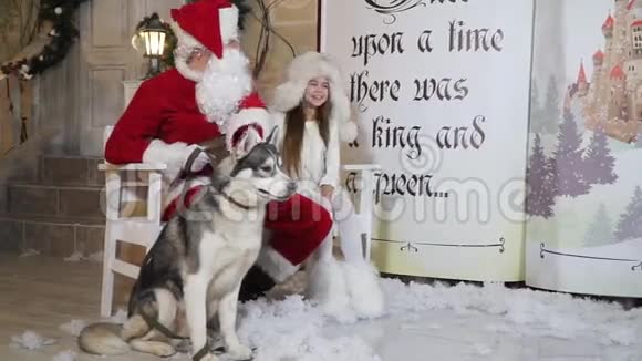 在门廊附近的长凳上坐着圣诞老人小女孩和狗莱卡视频的预览图