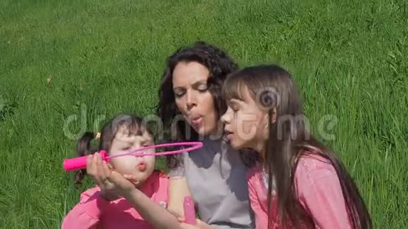 一个幸福的家庭在大自然中玩肥皂泡妈妈和女儿在阳光明媚的一天在绿色的草坪上玩耍有子女的女孩视频的预览图