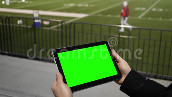 男子在露天看台的足球队练习赛上观看绿屏平板视频的预览图