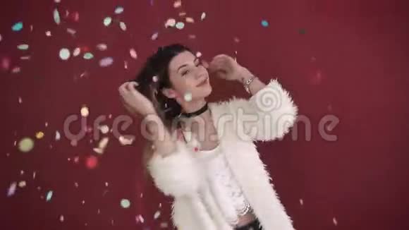 美丽的女孩在彩色纸屑中慢动作女人在红色背景下的纸屑中跳舞视频的预览图
