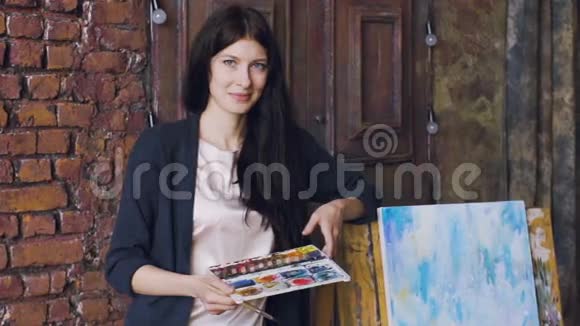 年轻女艺术家的慢镜头肖像站在完成的图片附近微笑进入相机视频的预览图