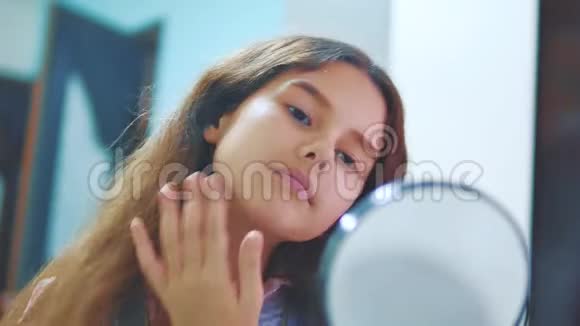 可爱的黑发西班牙小女孩在她的脸上涂奶油有趣的年轻女孩带着面具的皮肤儿童视频的预览图
