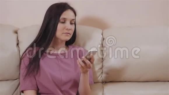 年轻的布鲁内特在家里的皮革沙发上的定位和电话交谈视频的预览图