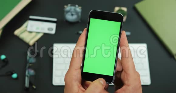 男人在工作桌上拿着绿色屏幕的智能手机敲着它的一些东西视频的预览图