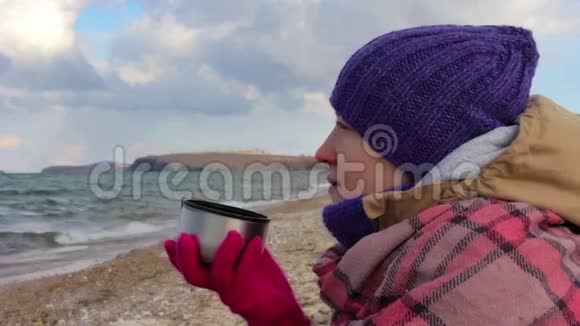 女孩坐在海边喝热茶波浪美丽的风景视频的预览图