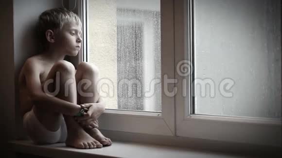 穆迪的小男孩坐在窗台上看着雨滴沿着窗户玻璃往下走视频的预览图