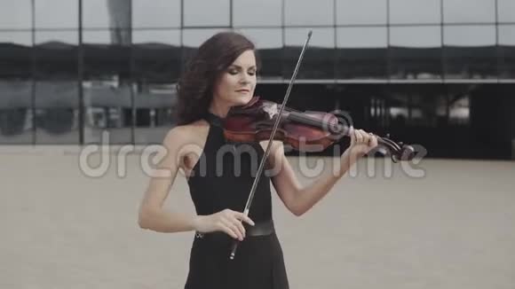 漂亮的小提琴手穿着黑色连衣裙靠近玻璃建筑城市艺术概念视频的预览图