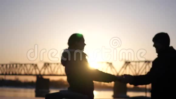 年轻的幸福夫妇牵着彼此手微笑着面对美丽的夕阳和铁路桥4k视频的预览图