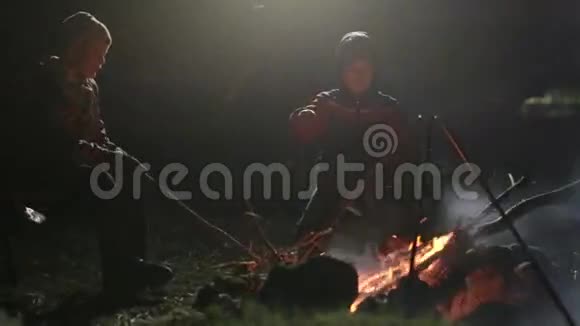 两个男孩晚上坐在篝火旁边纠正煤炭和交谈视频的预览图