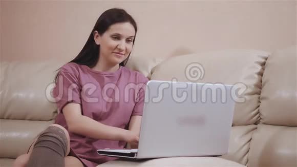 年轻的布鲁内特女孩在温暖的袜子躺在皮革沙发在家里和工作在笔记本电脑网上购物视频的预览图