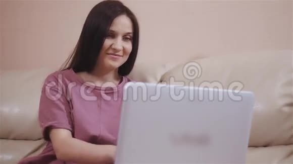 年轻的布鲁内特女孩在温暖的袜子躺在皮革沙发在家里和工作在笔记本电脑网上购物视频的预览图