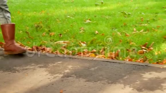 一个穿靴子的女孩在绿草和秋叶的背景下走上人行道视频的预览图