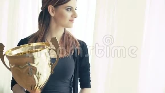 漂亮女孩的肖像带着金色的奖杯看着窗户4K视频的预览图