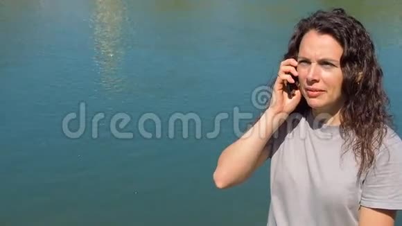 河边有电话的女孩在水附近的新鲜空气中移动自然的晴天视频的预览图