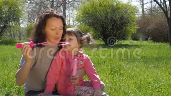 一个和她母亲在一起的孩子在玩肥皂泡野外的幸福家庭妈妈和女儿在吹泡泡视频的预览图