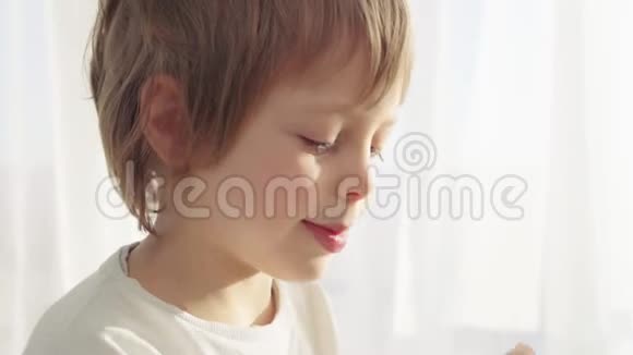 男孩在现代厨房吃早餐男孩吃带牛奶的饼干厨房里的白色桌子灰色碗在桌子上视频的预览图