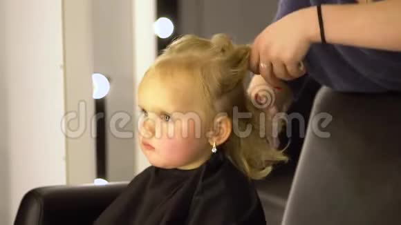 一个在美容院的小孩漂亮的女孩坐在椅子上理发师剪了她的头发孩子很困惑视频的预览图
