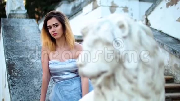 迷人的女孩黑色的眉毛和卷曲的头发银色和蓝色的裙子坐在石栏杆附近的狮子雕像和卷发视频的预览图