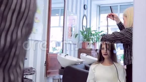 在一个漂亮的年轻模特在理发师工作时的镜子里的倒影视频的预览图