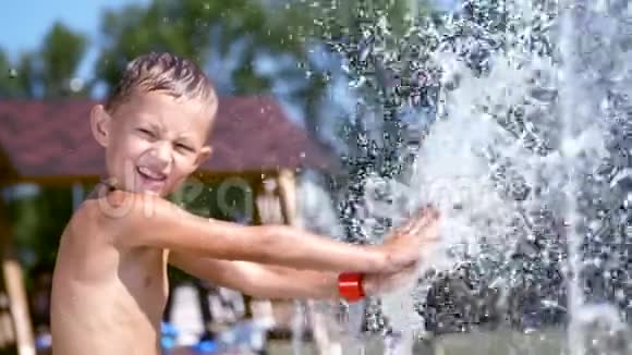 一个七岁的男孩穿着泳衣在喷泉里洗澡到处跑喷射玩得开心在炎热的夏天慢动作视频的预览图