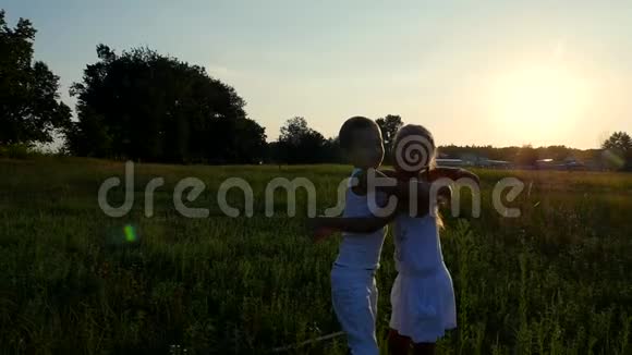 剪影儿童的身影男孩和女孩拥抱在太阳的背景下在日落的夏天快乐视频的预览图
