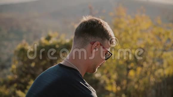 慢动作的英俊年轻时尚男士戴着太阳镜在田野里看着日落1920x1080特写视频的预览图