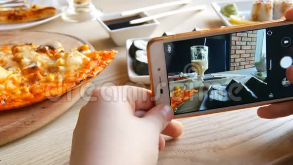 少年男孩在智能手机上拍一张食物的照片餐厅桌上有日本寿司卷和意大利披萨视频的预览图