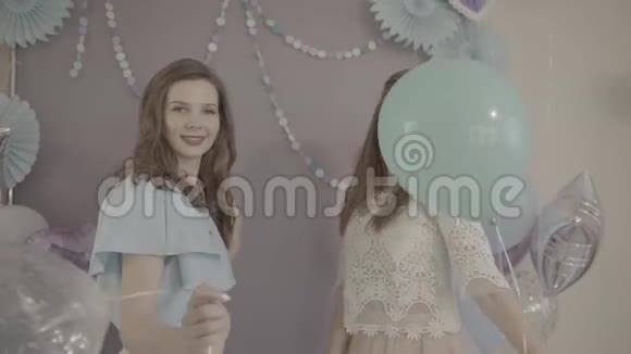 两个年轻的兴奋迷人的女人穿着漂亮的漂亮裙子手里拿着气球在镜头前微笑着转过身来视频的预览图