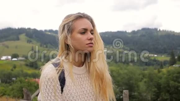 美丽的女孩在镜头前摆姿势在森林和山村的背景上微笑视频的预览图