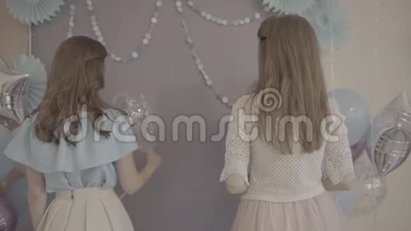 两个兴奋迷人的年轻女人穿着漂亮的漂亮裙子手里拿着气球在镜头前微笑着转过身来视频的预览图