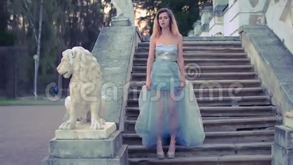 穿着银色和蓝色连衣裙穿着高跟鞋的漂亮女孩站在楼梯上石栏杆靠近狮子雕像视频的预览图