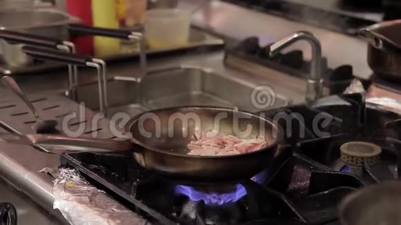 厨师在餐厅的厨房里用煤气火焰在煎锅里煮培根视频的预览图