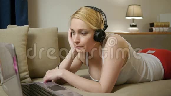 有笔记本电脑和耳机的女人躺在沙发上视频的预览图