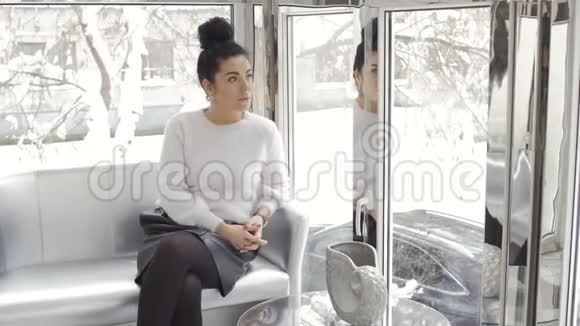 漂亮的女人坐在靠近窗户的沙发上视频的预览图