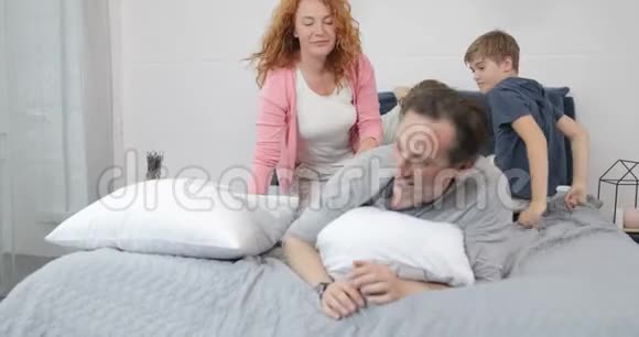 幸福的家庭在卧室孩子和父母的沟通躺在父亲床上早上视频的预览图