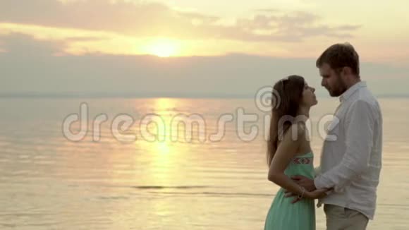 幸福的年轻夫妇站在日落的海滩上女朋友吻她男朋友视频的预览图