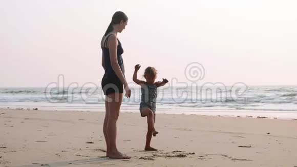 年轻的运动妈妈和小女儿在海滩上做体操视频的预览图