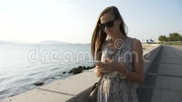 有智能手机的年轻女性在城市的海滨散步stealicam射击视频的预览图
