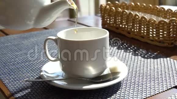 白茶壶慢慢地把茶倒进杯子里咖啡厅内部阳光视频的预览图