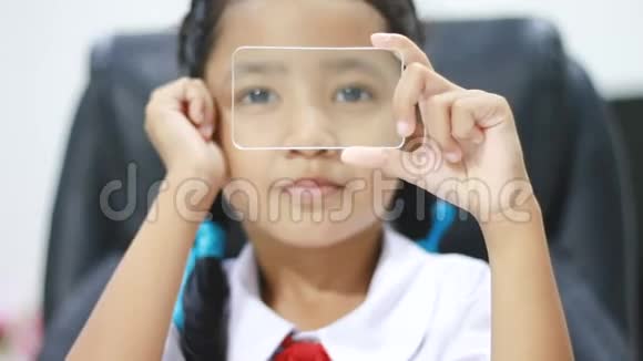 泰国幼儿园学生制服中的近镜头亚洲小女孩使用透明玻璃就像智能手机用于未来的网络视频的预览图