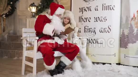 圣诞老人正在看童话故事小女孩坐在魔法书旁边视频的预览图