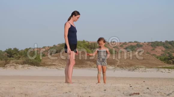 年轻的运动妈妈和小女儿在海滩上做体操视频的预览图