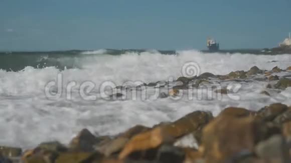 海浪拍打着海岸上的岩石背景上的货船视频的预览图